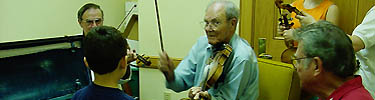 Experienced fiddlers explain bow technique to young musicians at the Prairie Acadian Cultural Center.
